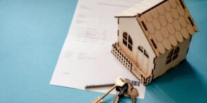 Maqueta de una casa sobre documentos de compraventa junto a unas llaves