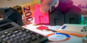 Casas en miniatura junto a billetes de euro y una calculadora