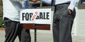 Apretón de manos entre vendedor y comprador junto a un cartel de propiedad vendida